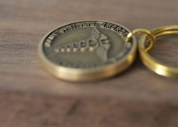 Close-up of a gold medical alert keychain on a wooden surface, engraved with a caduceus symbol and text.