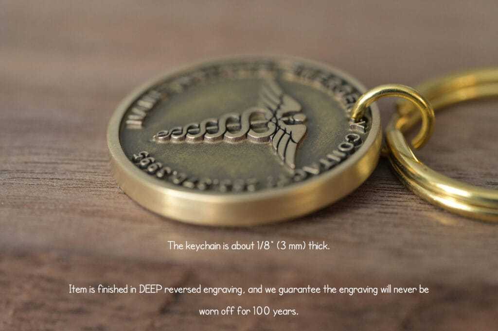 Close-up of a gold keychain with a deep engraved medical symbol and detailed text promising 100-year durability.