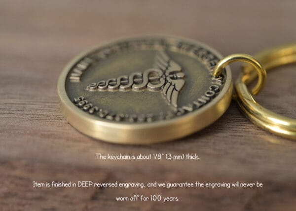 Close-up of a gold keychain with a deep engraved medical symbol and detailed text promising 100-year durability.