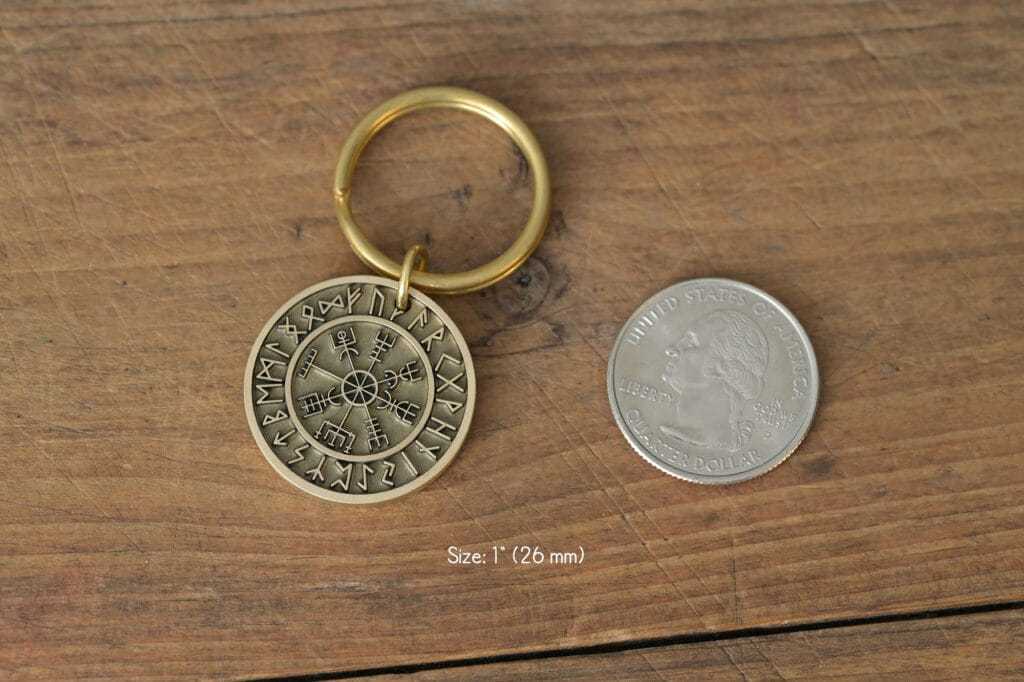 Viking rune keychain next to a U.S. quarter on wooden surface, showcasing size and detail.