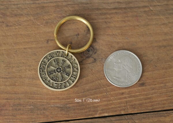 Viking rune keychain next to a U.S. quarter on wooden surface, showcasing size and detail.