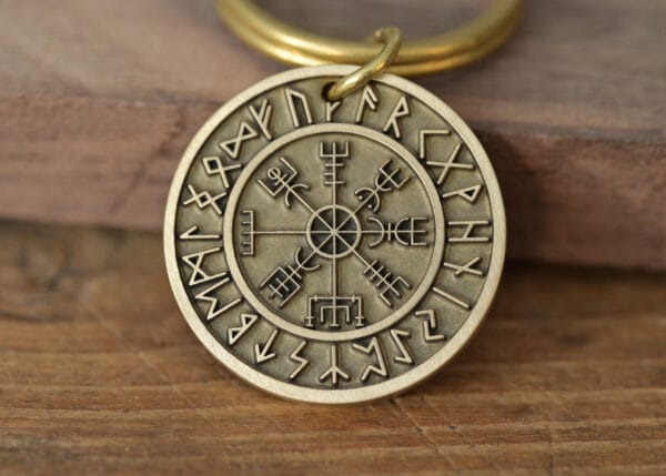 Close-up of a brass Viking runic pendant with ancient symbols on a wooden surface.