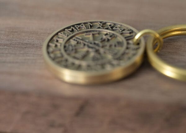 Close-up of an ancient brass coin keychain with intricate engravings on a wooden surface.
