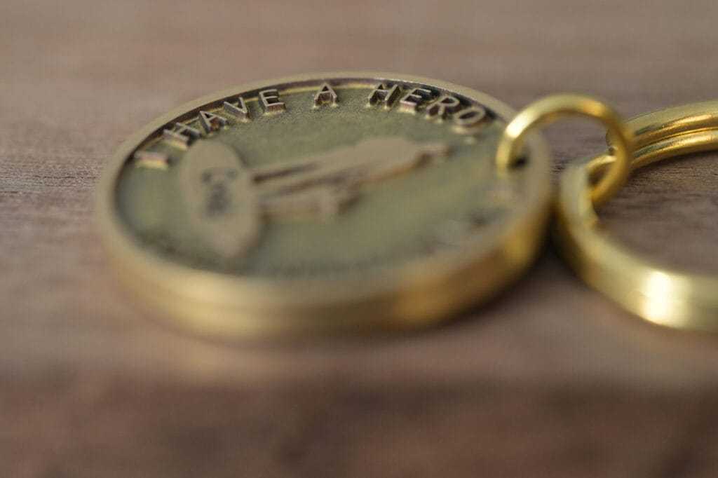 Close-up of a gold keychain with embossed text I Have a Hero, resting on a wooden surface.