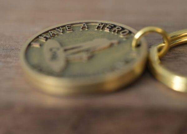 Close-up of a gold keychain with embossed text I Have a Hero, resting on a wooden surface.