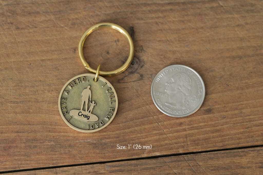 Personalized dad keychain with I Have a Hero, I Call Him Dad inscription, size comparison with a US quarter.
