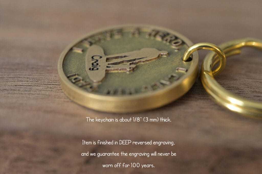 Close-up of a bronze keychain with deep reversed engraving, promised to last 100 years, on a wooden surface.