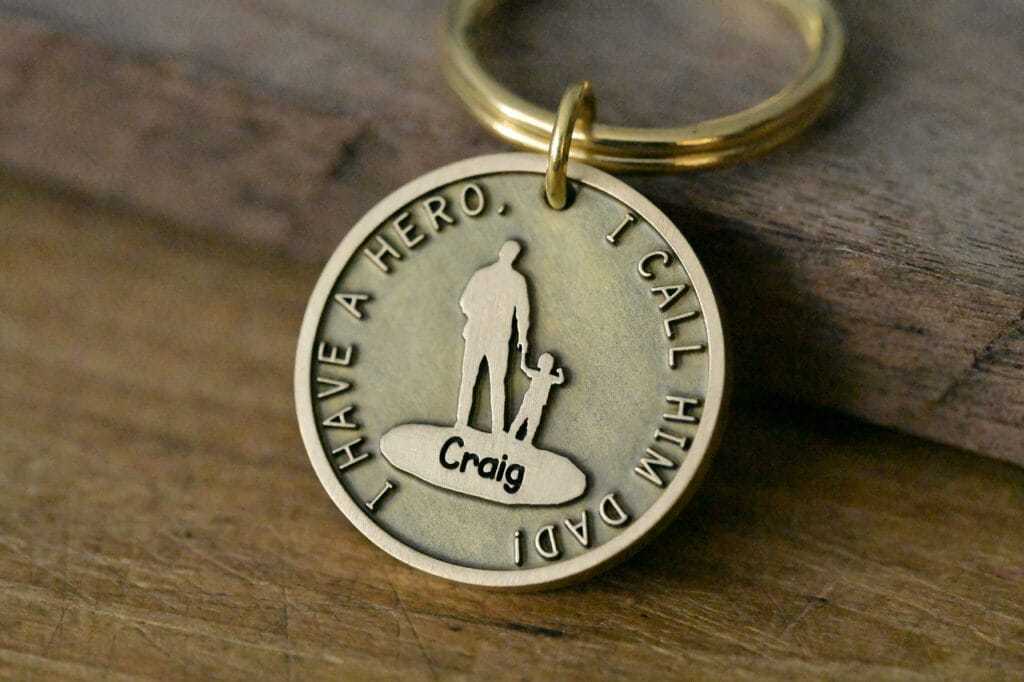 Gold keychain with engraved message I Have a Hero, I Call Him Dad, featuring silhouettes of a man and child.