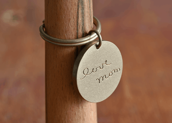 Engraved metal keychain with love mom hanging from a wooden pole, perfect personalized gift for Mother's Day.