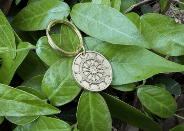 Gold steering wheel keychain on bright green leaves, symbolizing adventure and exploration in nature.