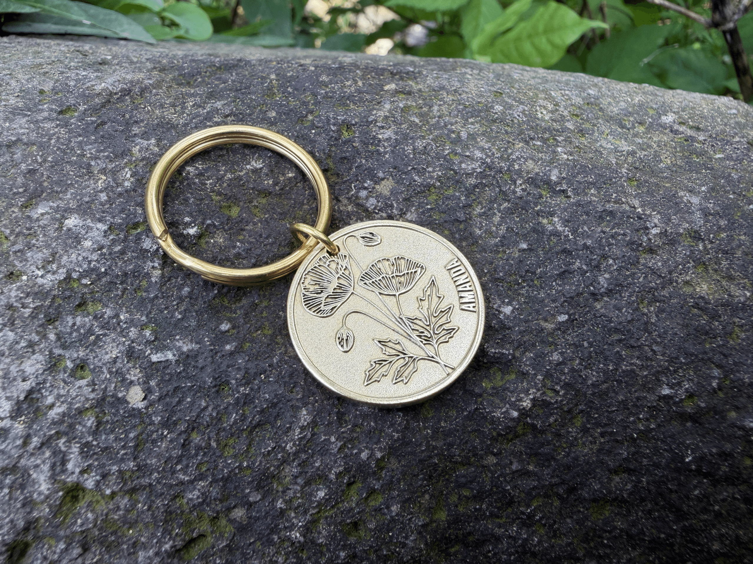 Gold keychain on rock with engraved poppy flower and the name AMANDA.
