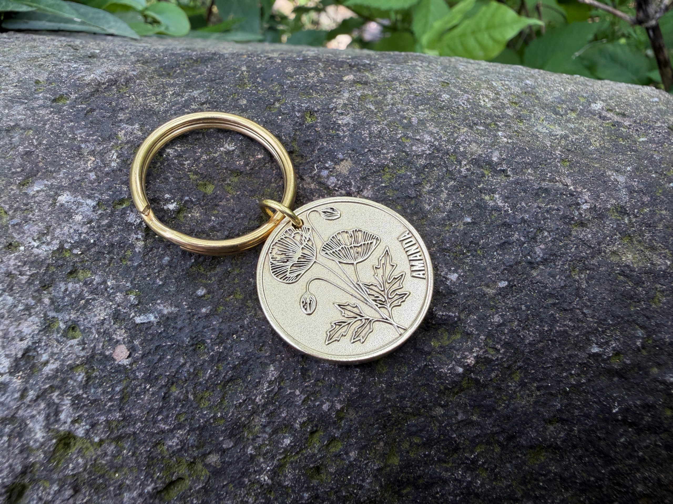 Gold keychain on rock with engraved poppy flower and the name AMANDA.