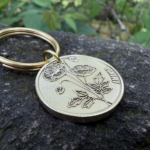 Keychain with engraved poppy flower and Amanda on a metal disc, placed on a rock surface.