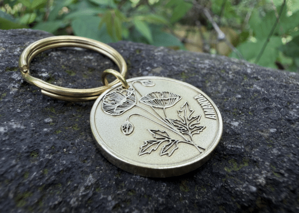 Keychain with engraved poppy flower and Amanda on a metal disc, placed on a rock surface.