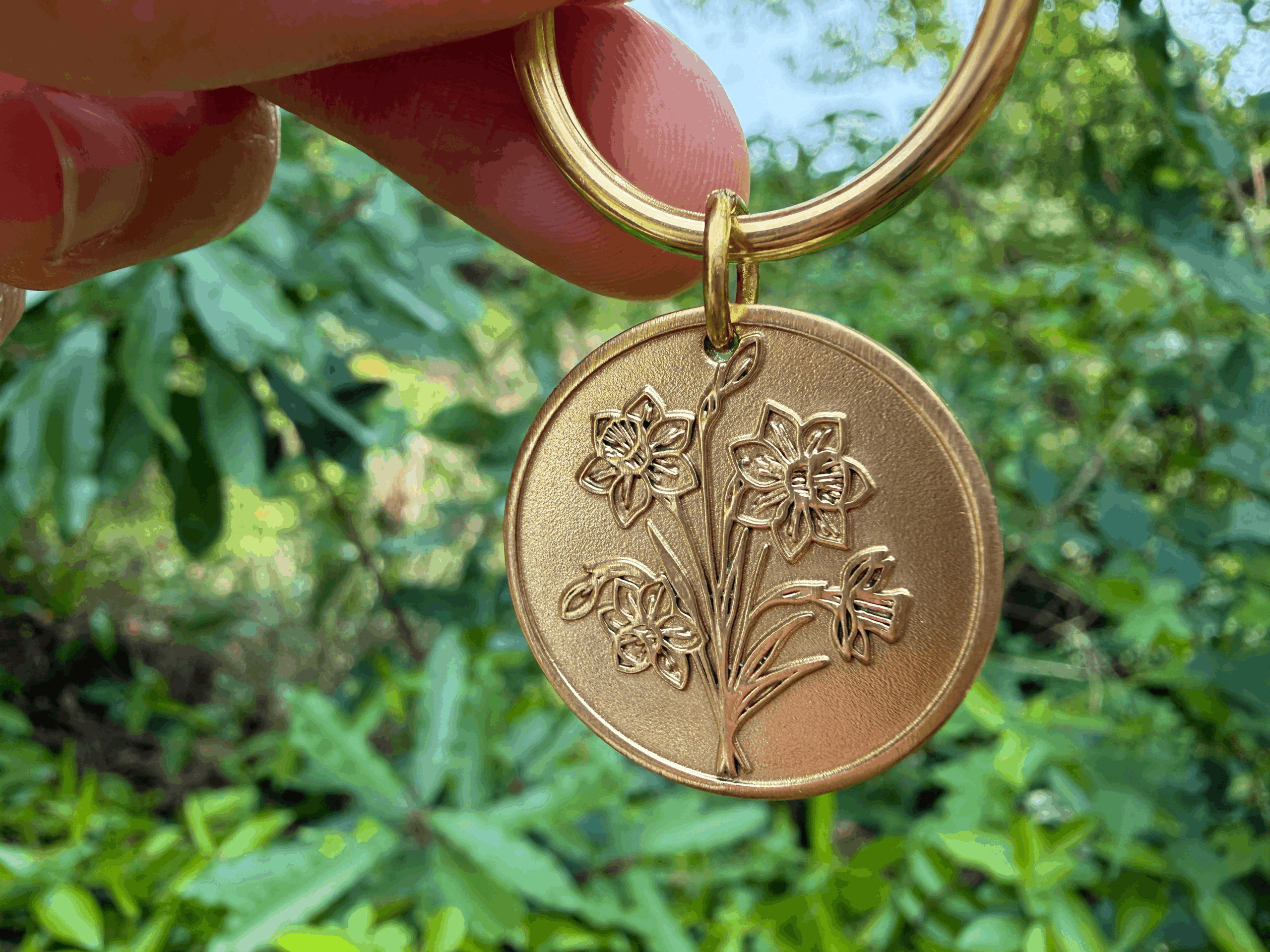 Gold flower-engraved pendant keychain against a lush green background.