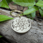 Keychain with engraved atom symbol on log with leaves; customizable text area Text Here.