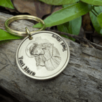 Keychain with engraved image of Jesus wearing a crown of thorns, placed on rustic wood with green leaves background.