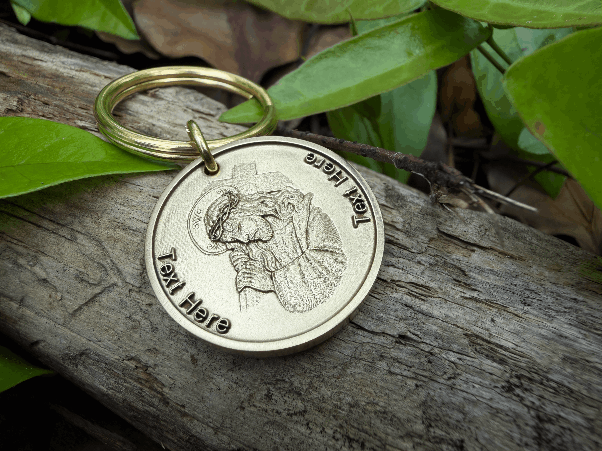 Keychain with engraved image of Jesus wearing a crown of thorns, placed on rustic wood with green leaves background.