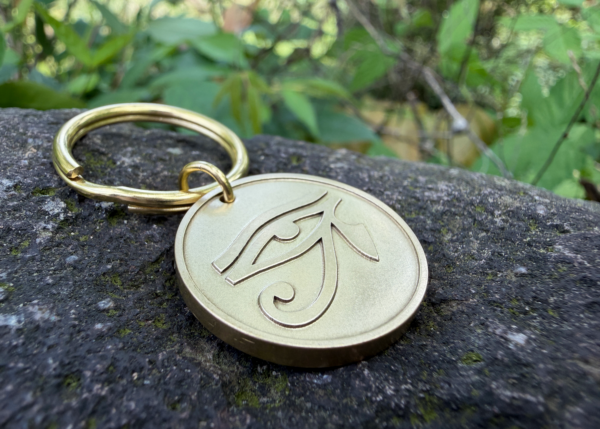 Golden keychain with Eye of Horus engraving on rock surface, surrounded by greenery in the background.