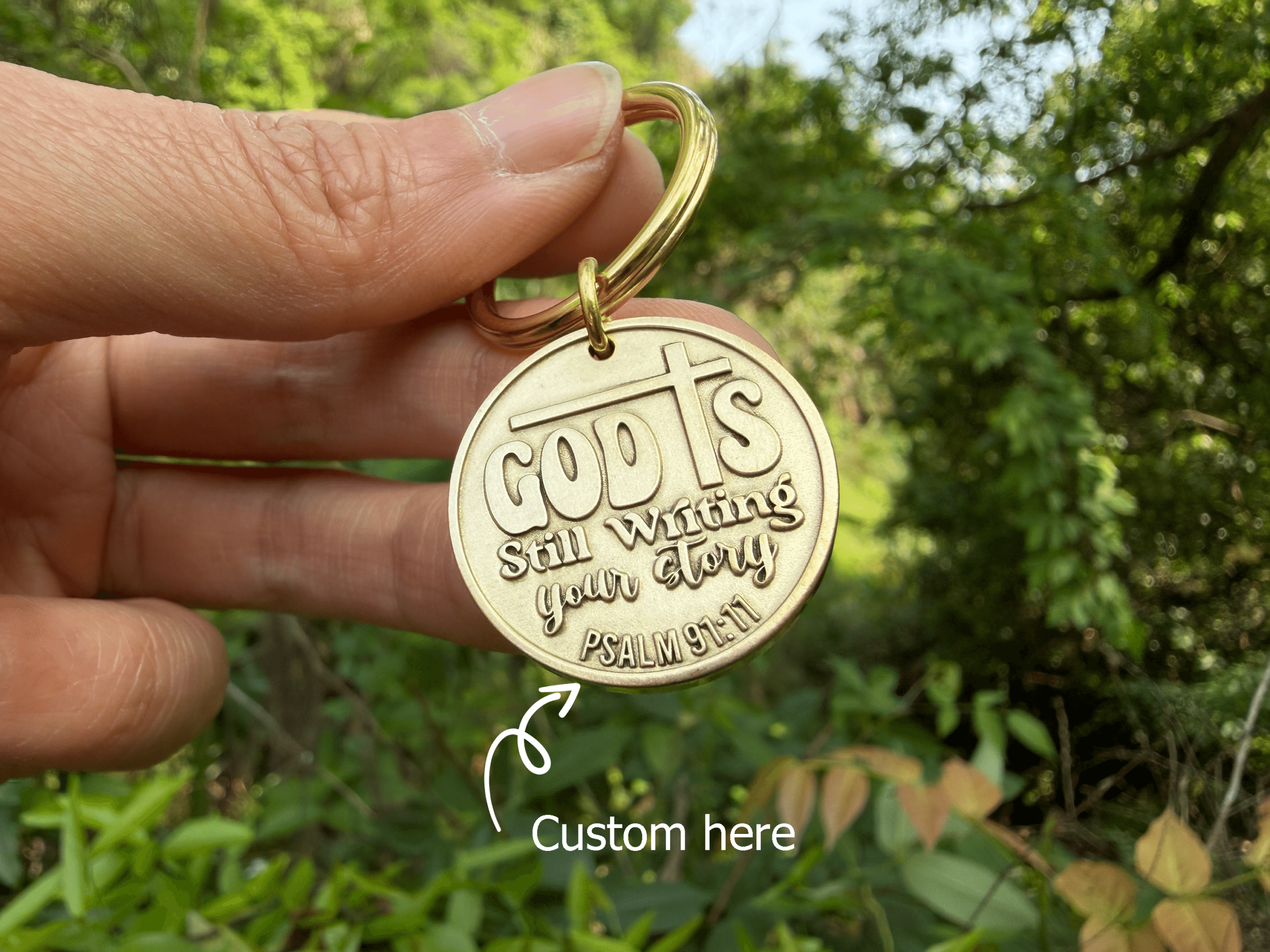 Keychain with God is still writing your story engraved, held in hand, nature background, Psalm 91:11 reference.