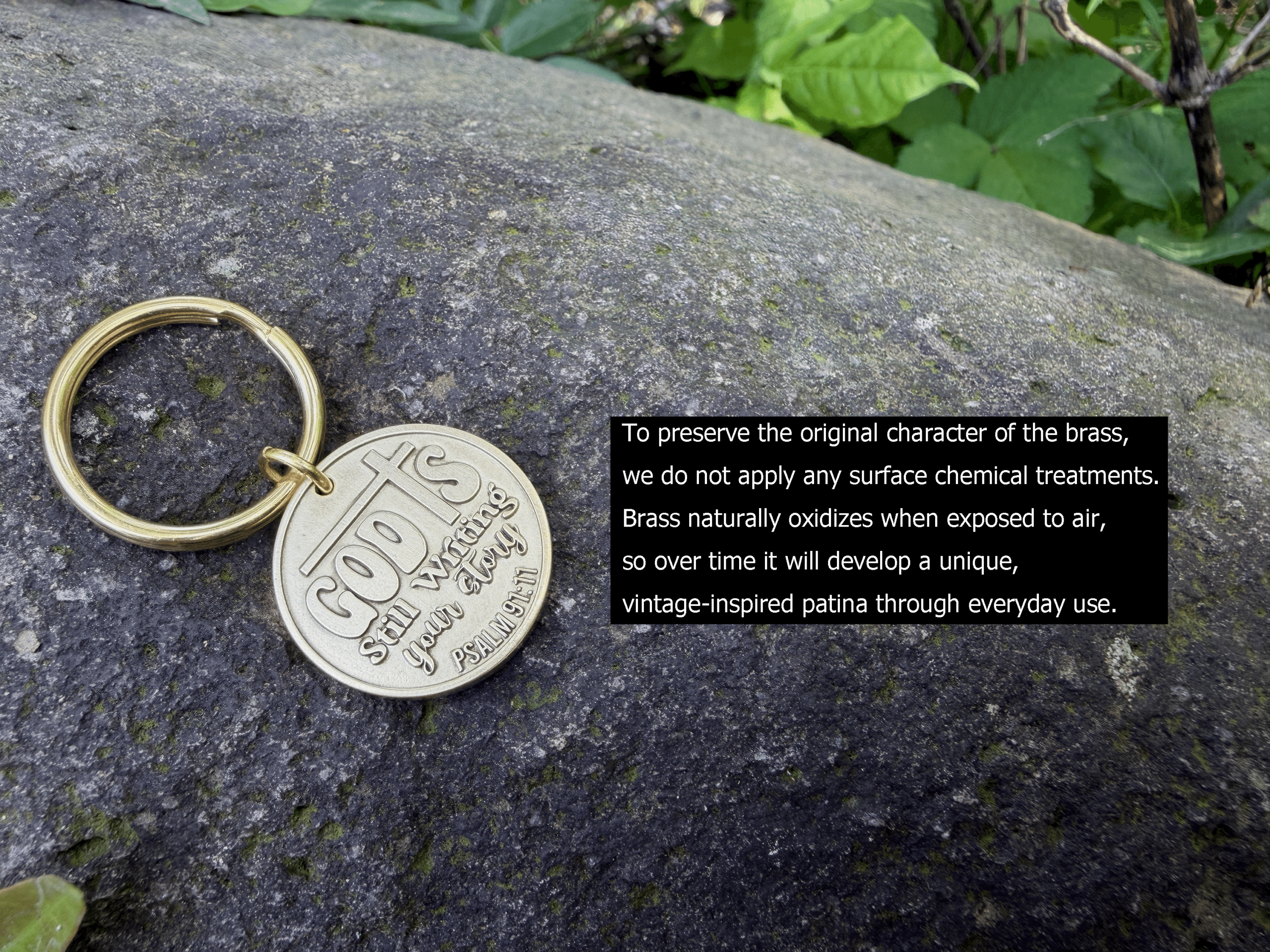 Brass keychain on rock engraved with God's still writing your story. Psalm 139:16 and oxidization message.