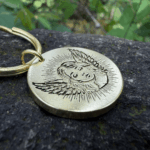 Gold keychain with an engraving of a baby angel on a textured stone surface.