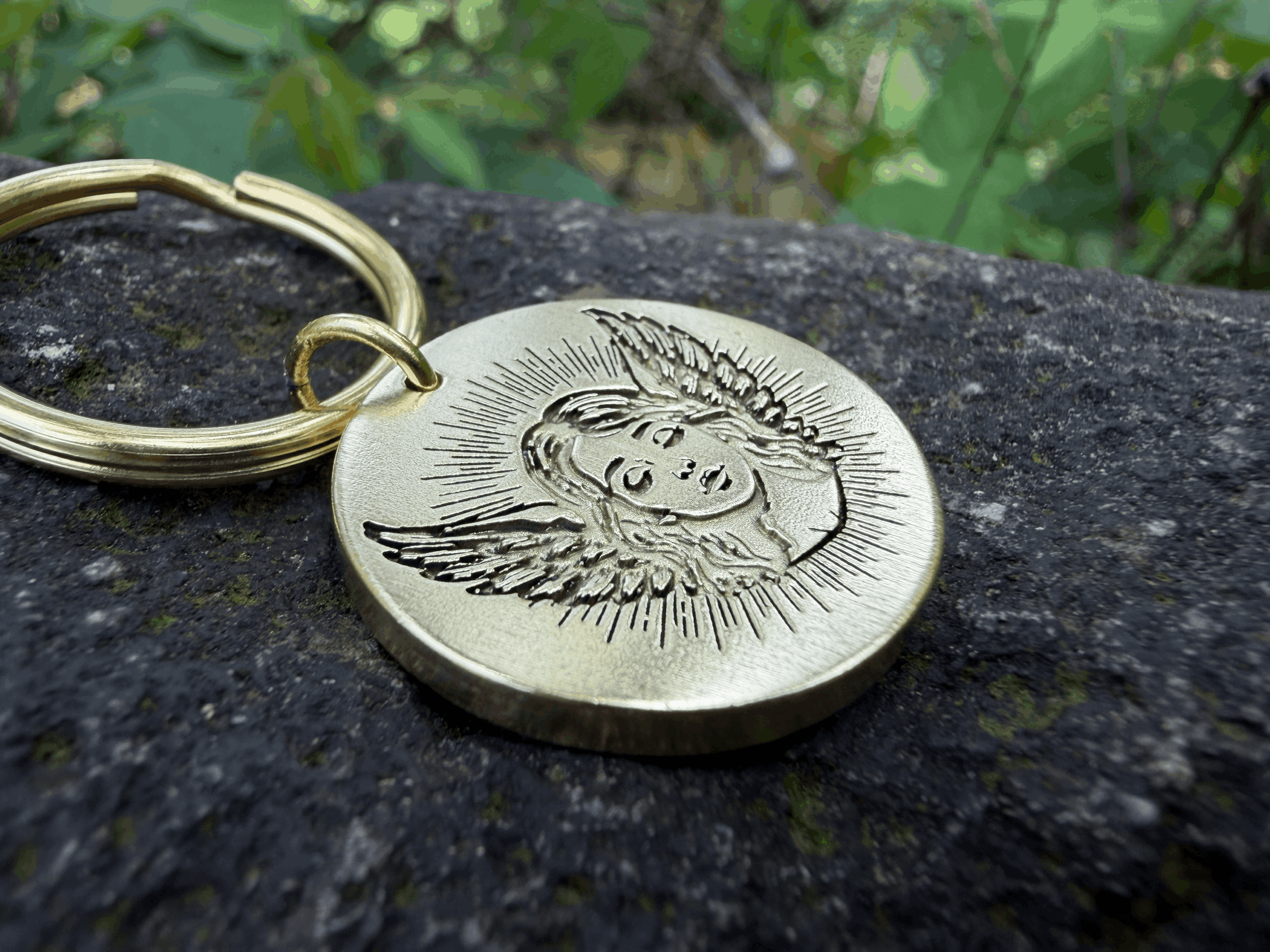 Gold keychain with an engraving of a baby angel on a textured stone surface.