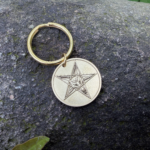 Gold keychain with Baphomet pentagram engraving on stone background.
