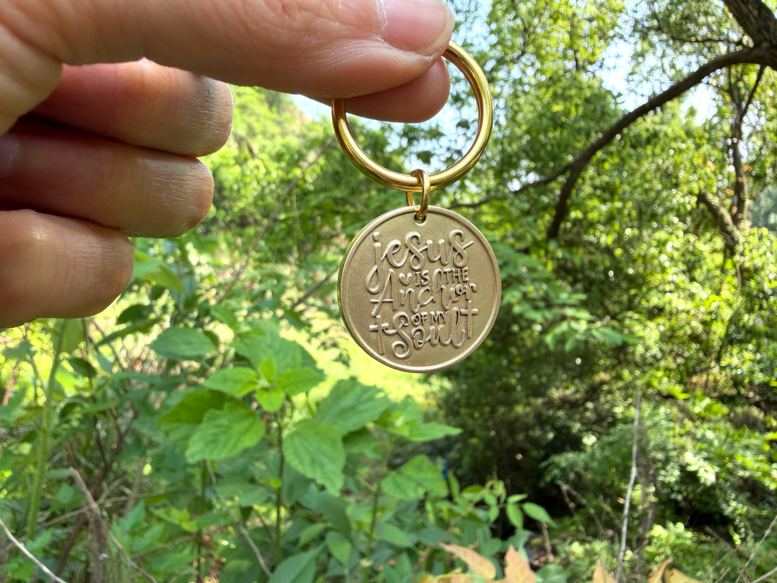 Keychain with Jesus is the anchor of my soul engraving, held outdoors against green foliage background.