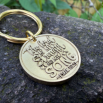 Gold keychain engraved with The Lord is my strength and my song - Psalm 118:14 on a stone background.