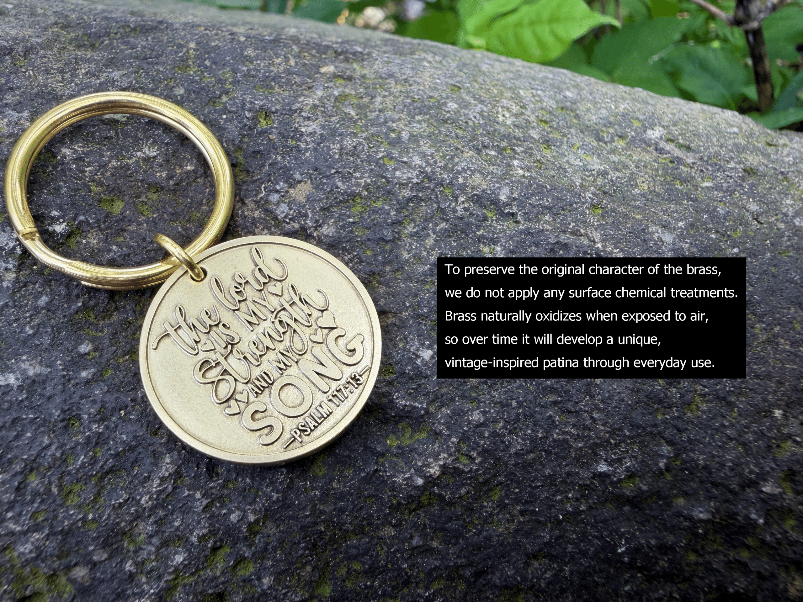 Brass keychain engraved with The Lord is my strength and my song, Psalm 117:13 on a stone background.