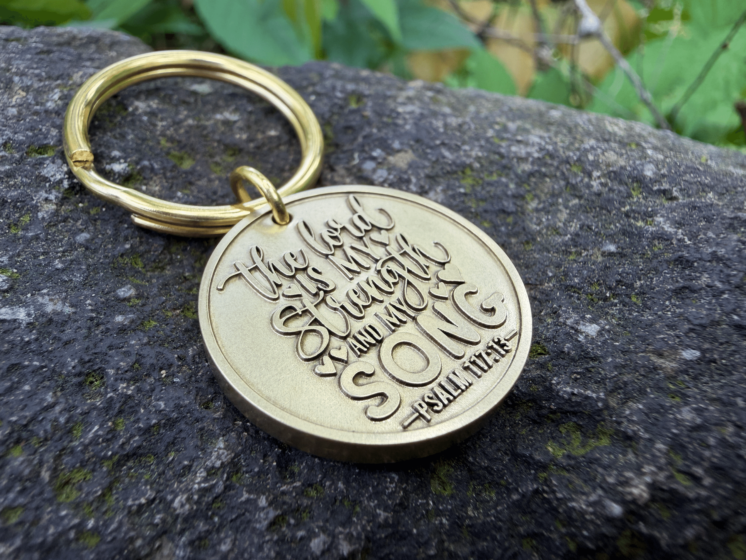 Gold keychain engraved with The Lord is my strength and my song - Psalm 118:14 on a stone background.
