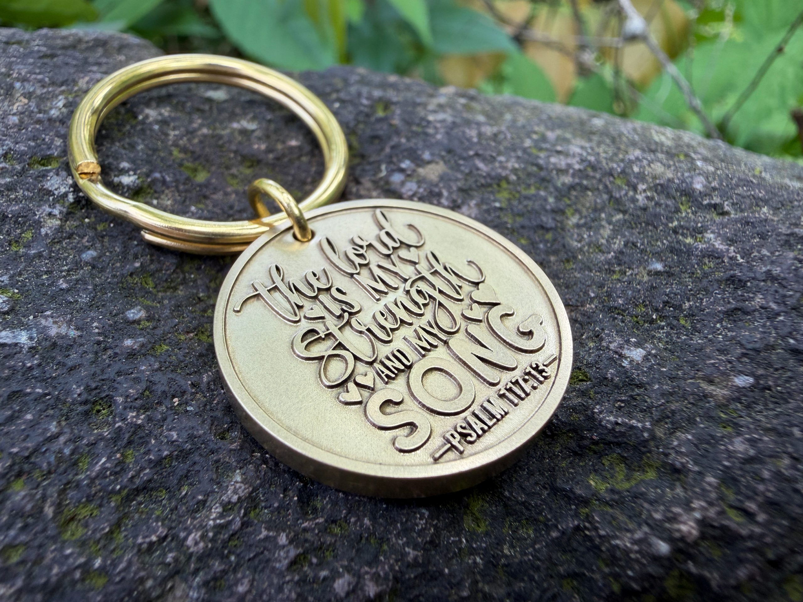 Gold keychain engraved with The Lord is my strength and my song - Psalm 118:14 on a stone background.