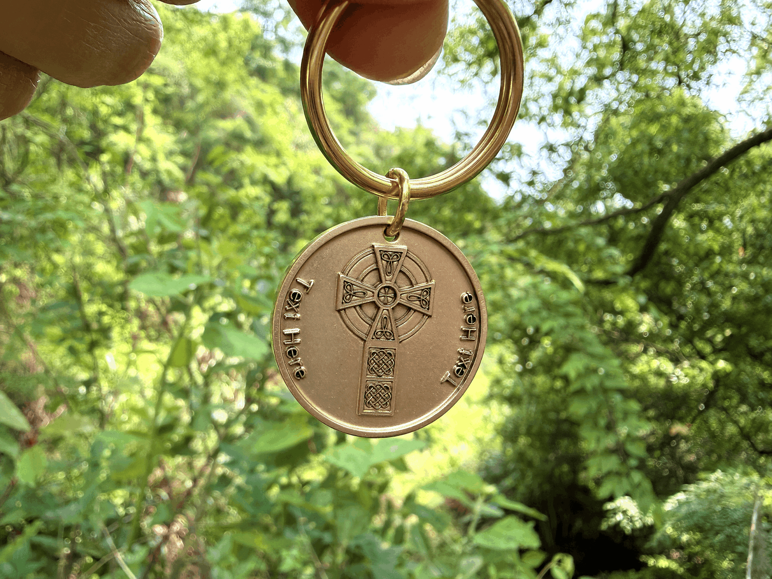 Bronze coin-shaped keychain with Celtic design held outdoors against lush green background.