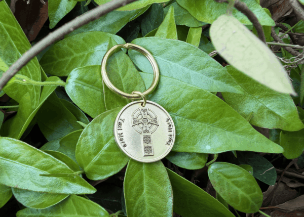 Personalized keychain with engraved cross design on vibrant green leaves background.