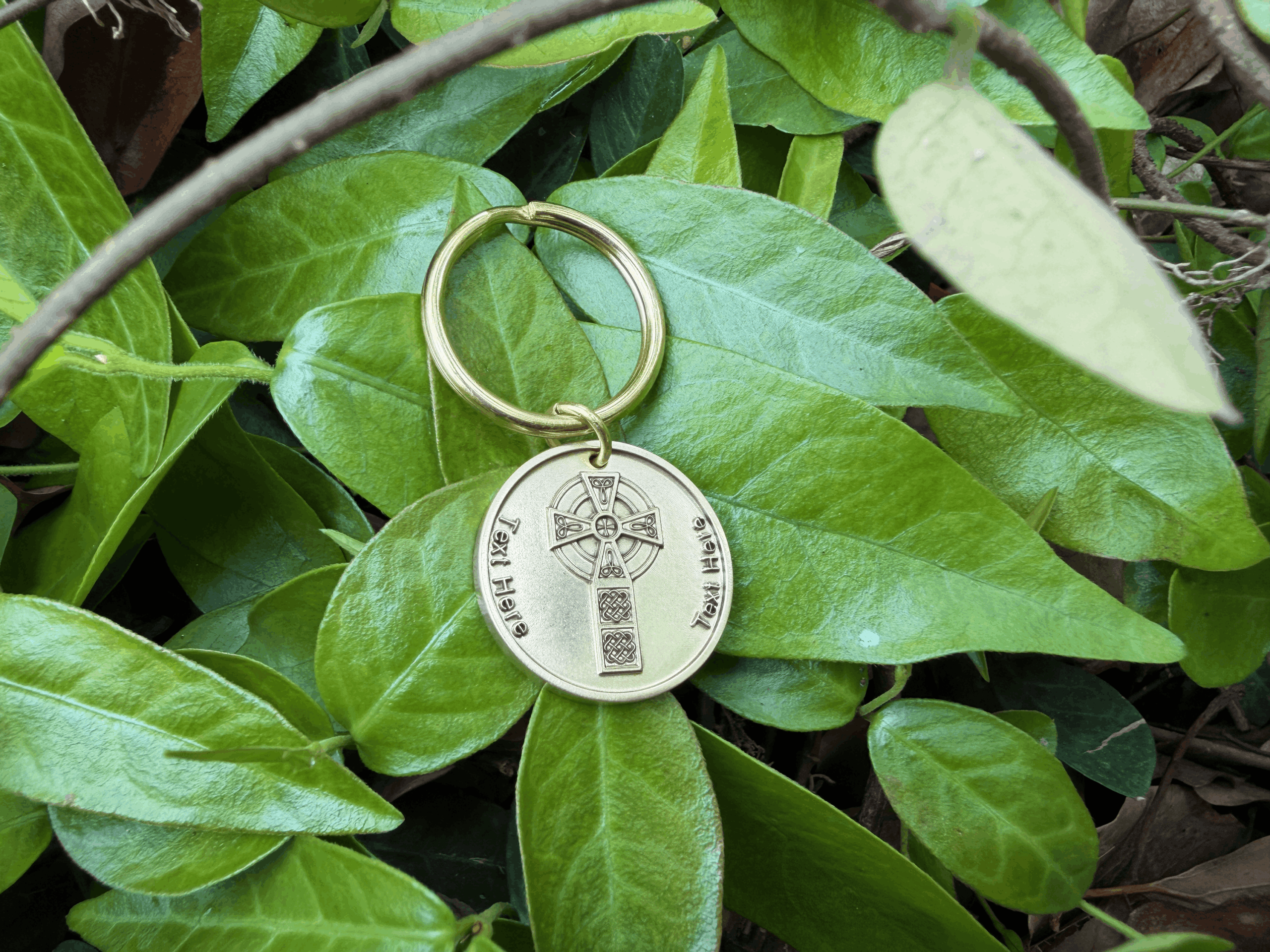 Personalized keychain with engraved cross design on vibrant green leaves background.