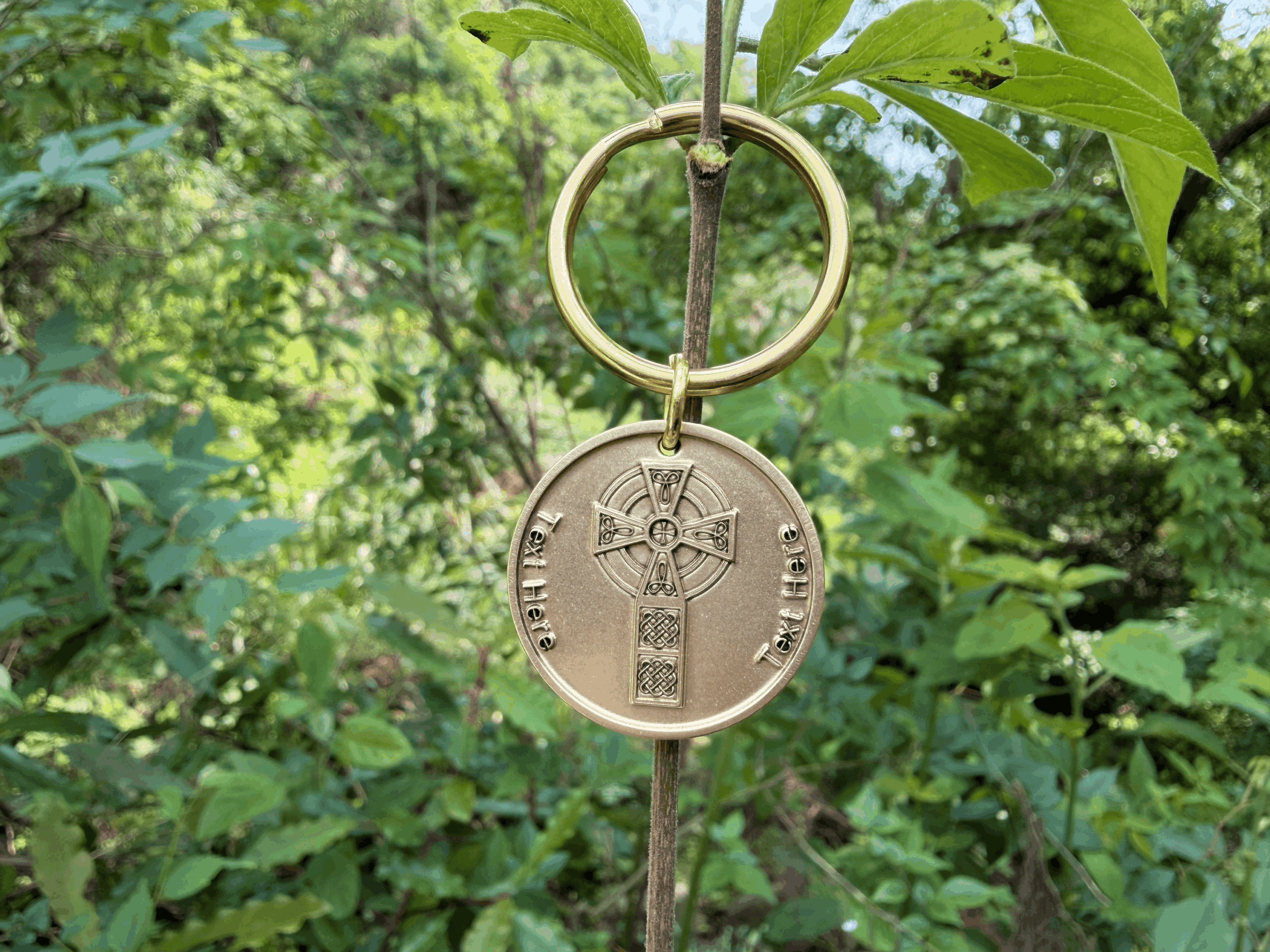 Personalized Brass Celtic cross keyring hanging on a branch with vibrant green leaves in the background.