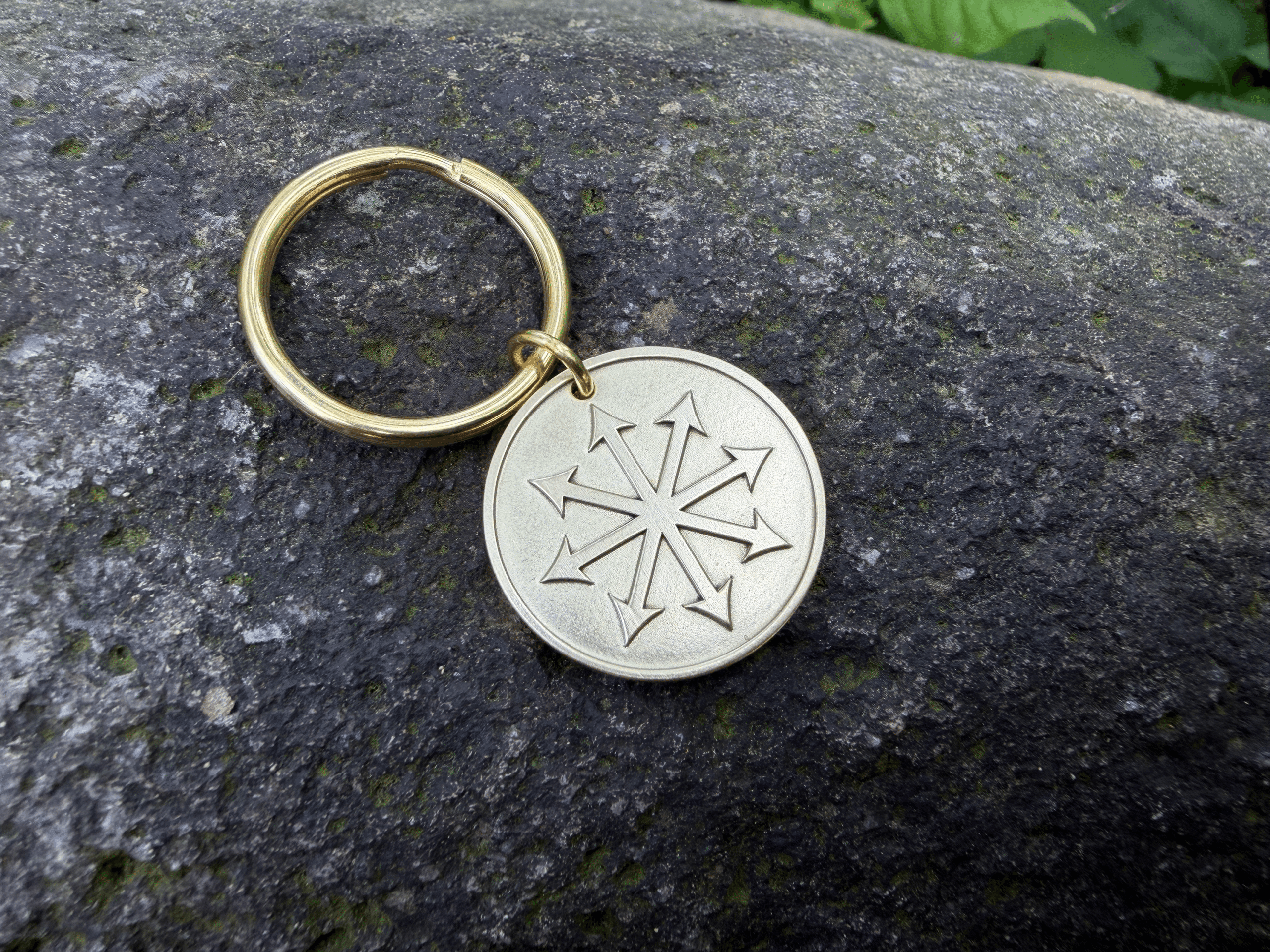 Keychain on rock with Chaos Star engraving, featuring eight arrows pointing outward.