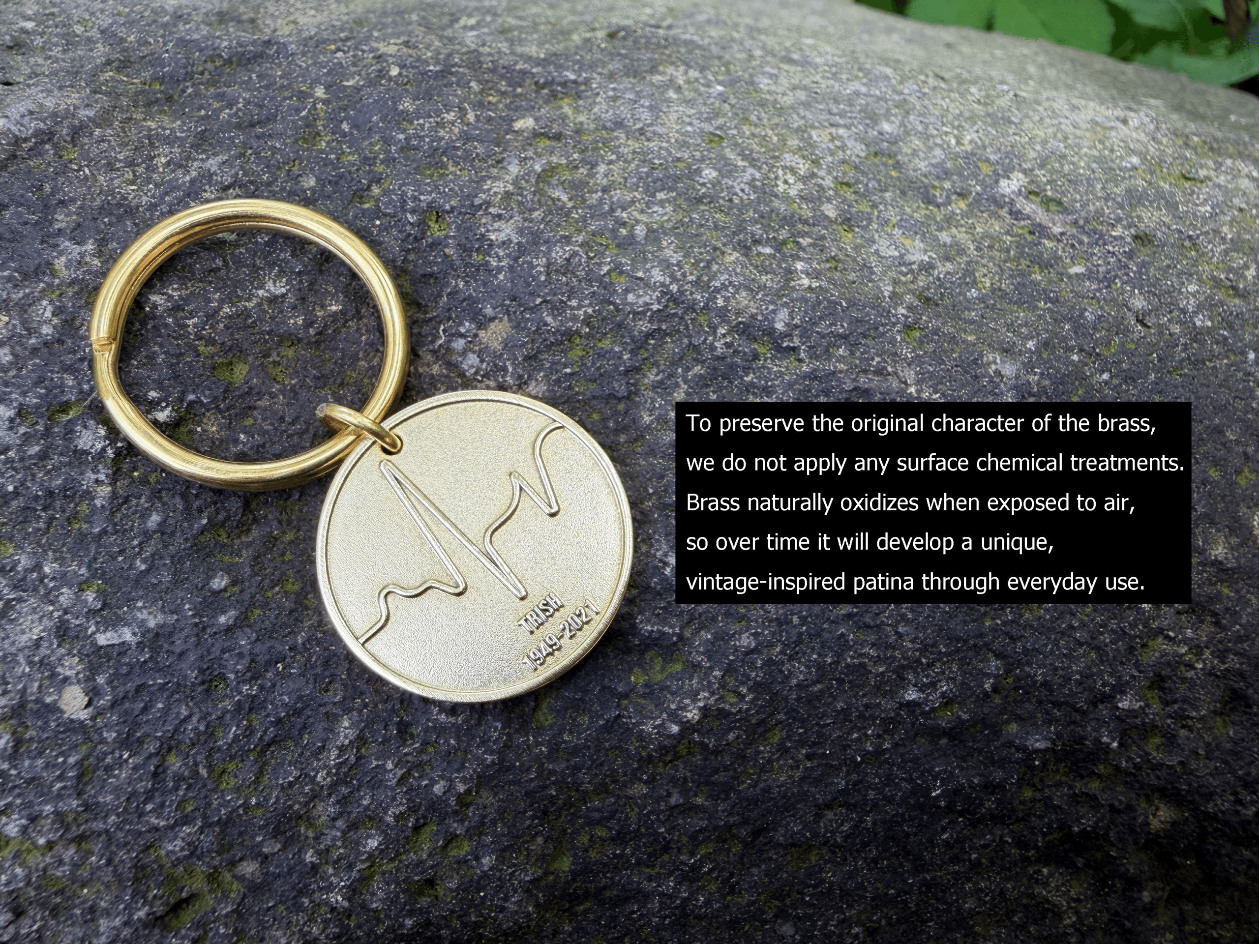 Brass keychain on a rock with engraved soundwave and text Inis E 1949-2021, highlighting natural oxidation process.