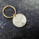 Gold keychain with wave engraving and text IRISH 1949-2021 on a stone surface.