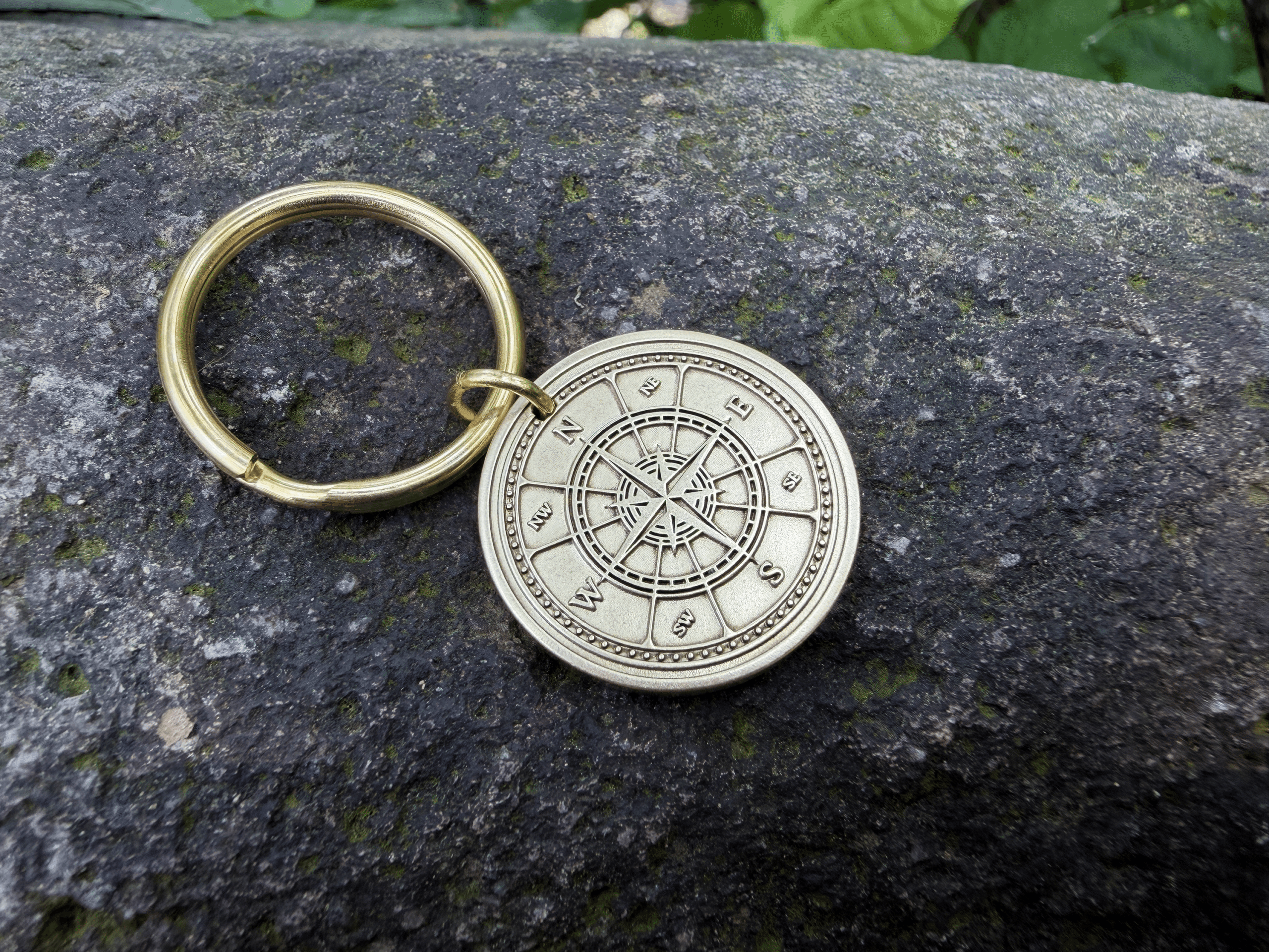 Gold keyring on stone with a compass rose engraving showing cardinal directions N, E, S, W for navigation.