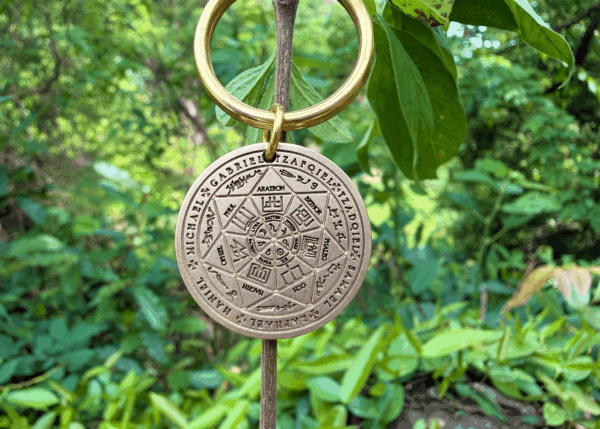 Personalized Seven Archangels keychain hanging from branch, surrounded by lush green leaves in a natural setting.