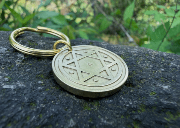Gold keychain with Star of David engraving resting on a stone, surrounded by greenery.