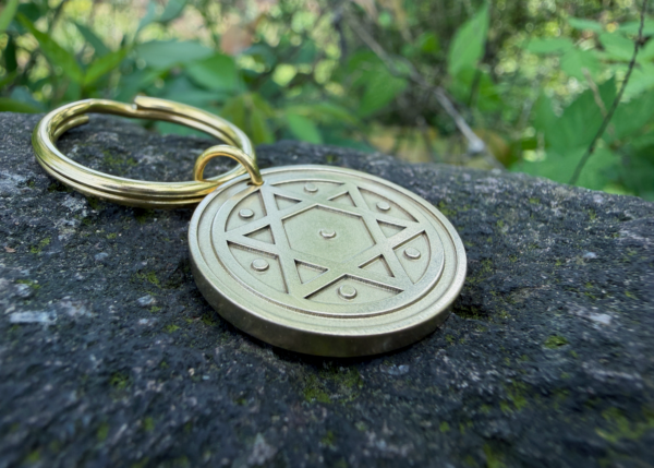 Gold keychain with Star of David engraving resting on a stone, surrounded by greenery.