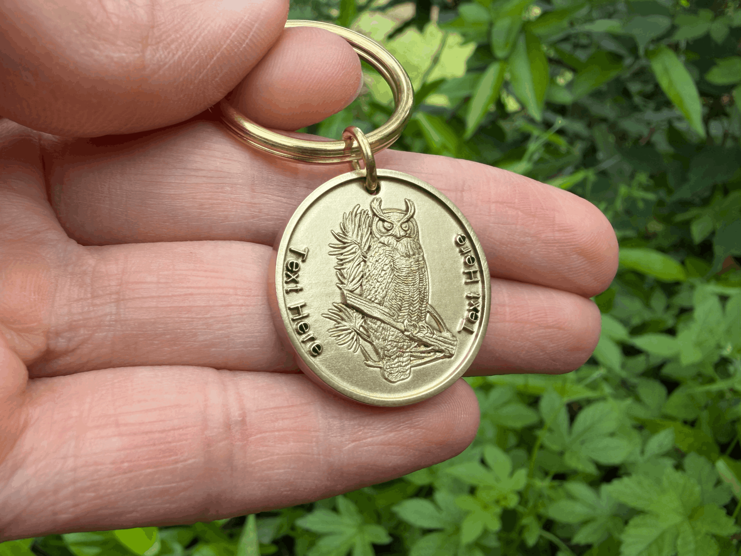 Close-up of a hand holding a brass keychain featuring an engraved owl design, with Text Here placeholder.