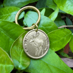 Gold keychain with a moose design resting on vibrant green leaves.