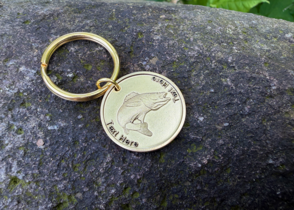 Gold keychain with engraved fish design on a rock surface, customizable text for branding or personalization.