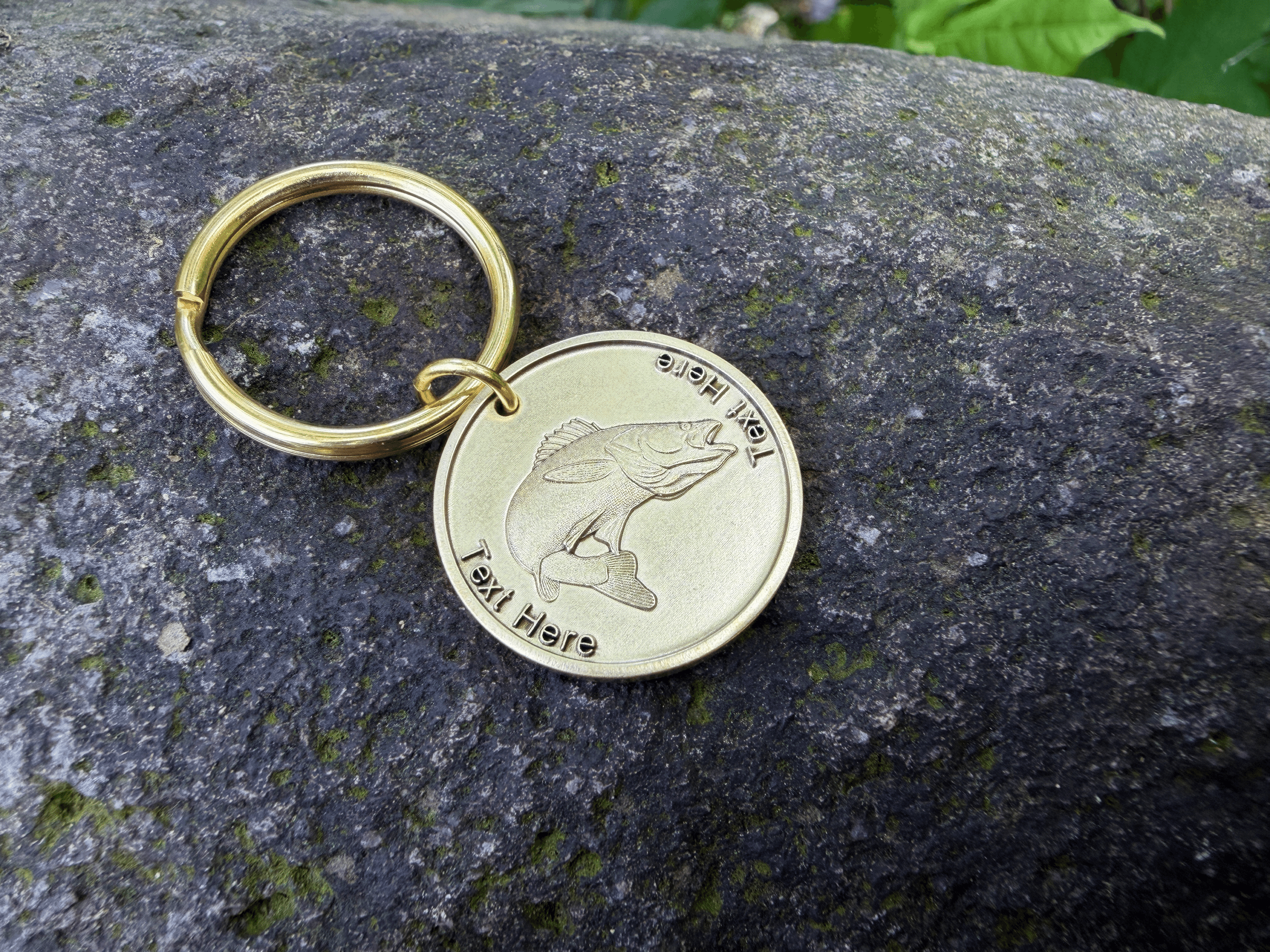 Gold keychain with engraved fish design on a rock surface, customizable text for branding or personalization.