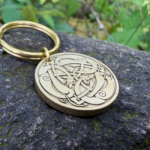 Celtic knot engraved keychain on stone with intricate loops and swirls design, gold finish, natural background.