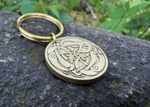 Celtic knot engraved keychain on stone with intricate loops and swirls design, gold finish, natural background.
